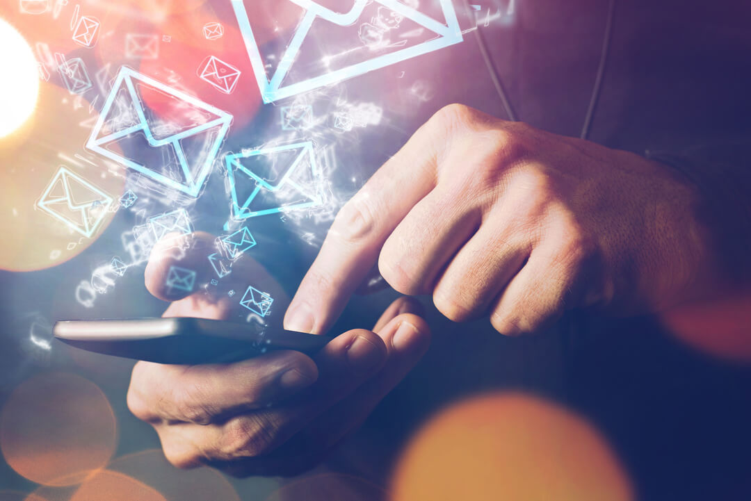 En mobiltelefon där någon trycker på skärmen och det i luften runtomkring flyger runt tecknade brev-ikoner.