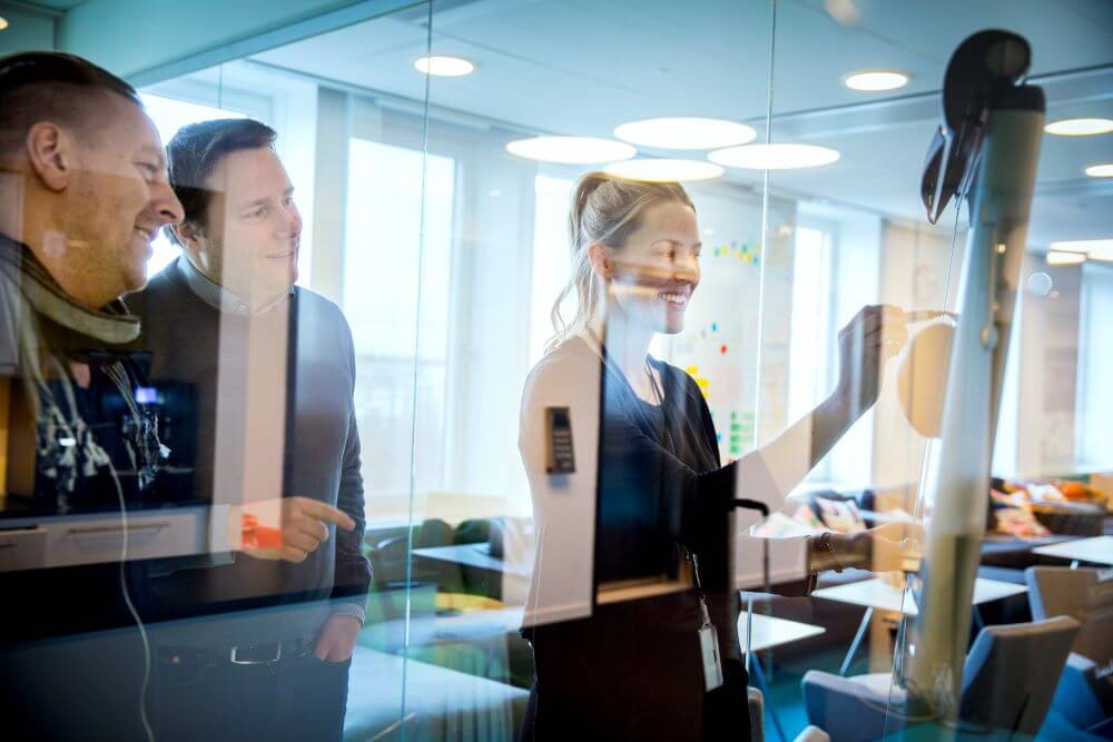 Tre personer som står framför en glasvägg i ett workshop-sammanhang.