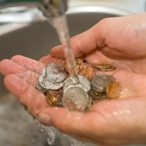 Händer med mynt i under en kran med rinnande vatten.