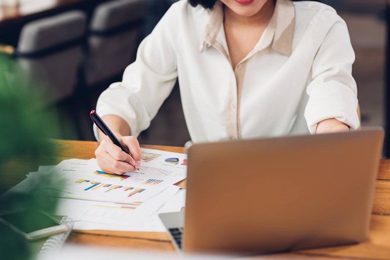 Person som sitter framför en dator och gör anteckningar på utskrivna papper.