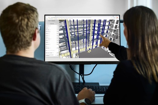 Två personer som tittar på en skärm som visar byggnadsinformation, där den ena personen pekar mot något på skärmen.