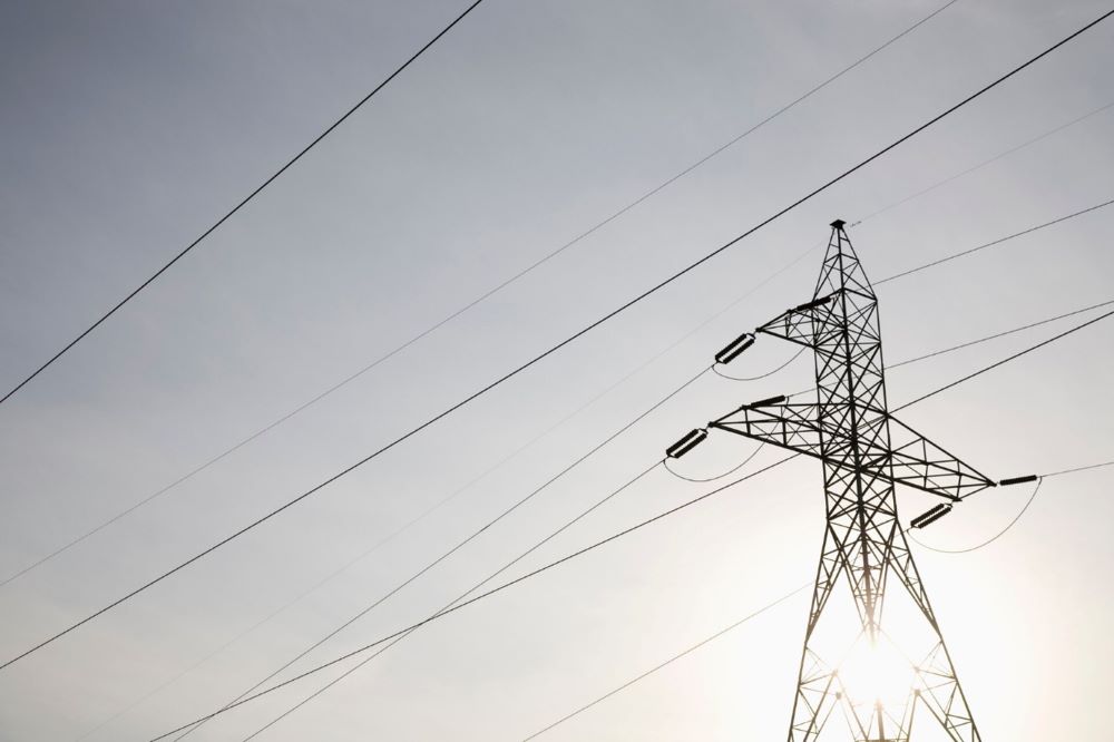 Toppen av en kraftledningsstolpe med kraftledningar runtomkring mot en ljus himmel.