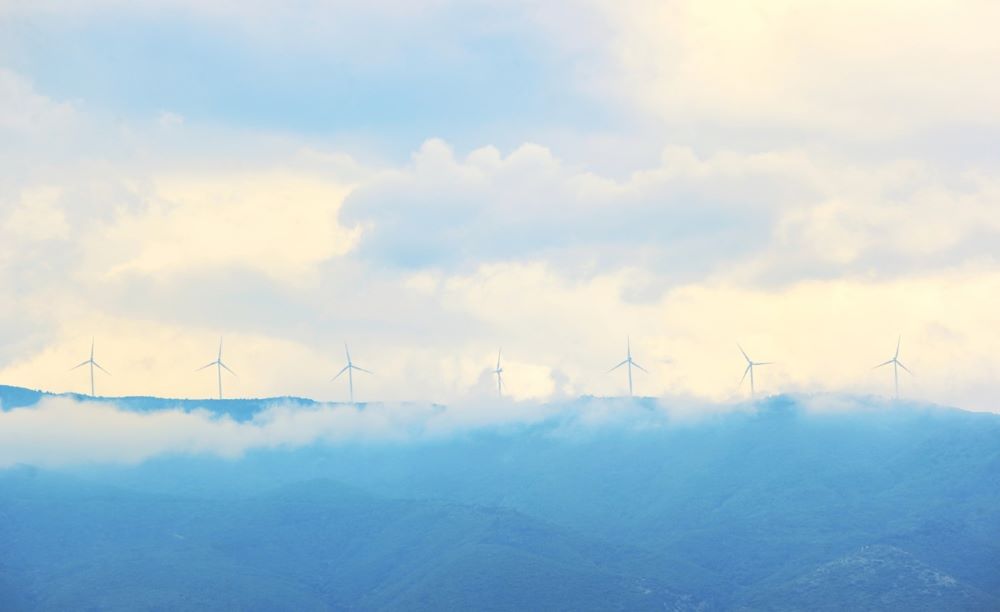 Vindkraftverk på en dimmig bergstopp under en molnig himmel.