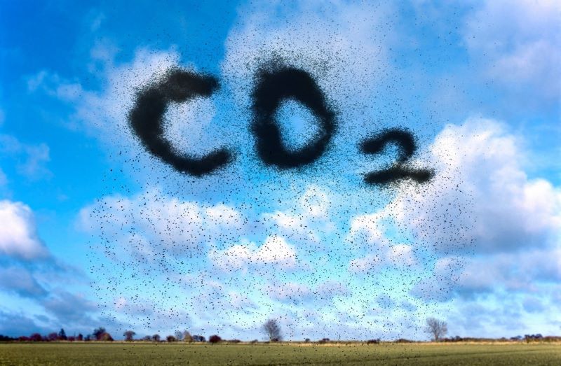 En bild av himlen där moln och partiklar formar texten "CO2" ovanför ett landskap.