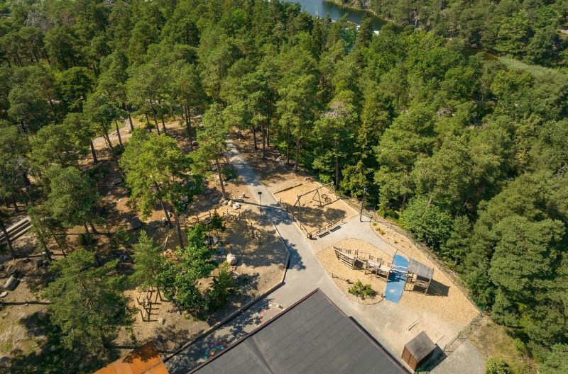 Flygfoto över skogsområde med Viktor Rydbergs skola i Nacka kommun, med en vik som skymtas i bakgrunden.