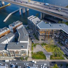 Flygfoto över moderna bostadshus på Bryggvägen, Gröndal i Stockholm, vid vattnet med innergård, intill en motorvägsbro och kaj.