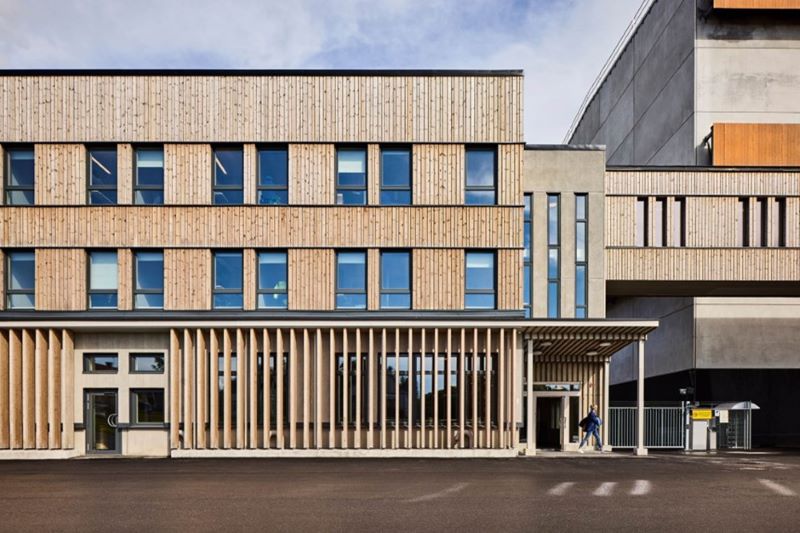 Modern byggnad med träfasad, stora fönster och entréparti i dagsljus.