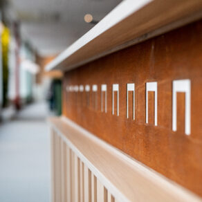 Detalj av foajé inredd med 100 procent återbruk: närbild på återbrukad trä- och metallpanel med utskurna grafiska former i en ljus, modern korridor.