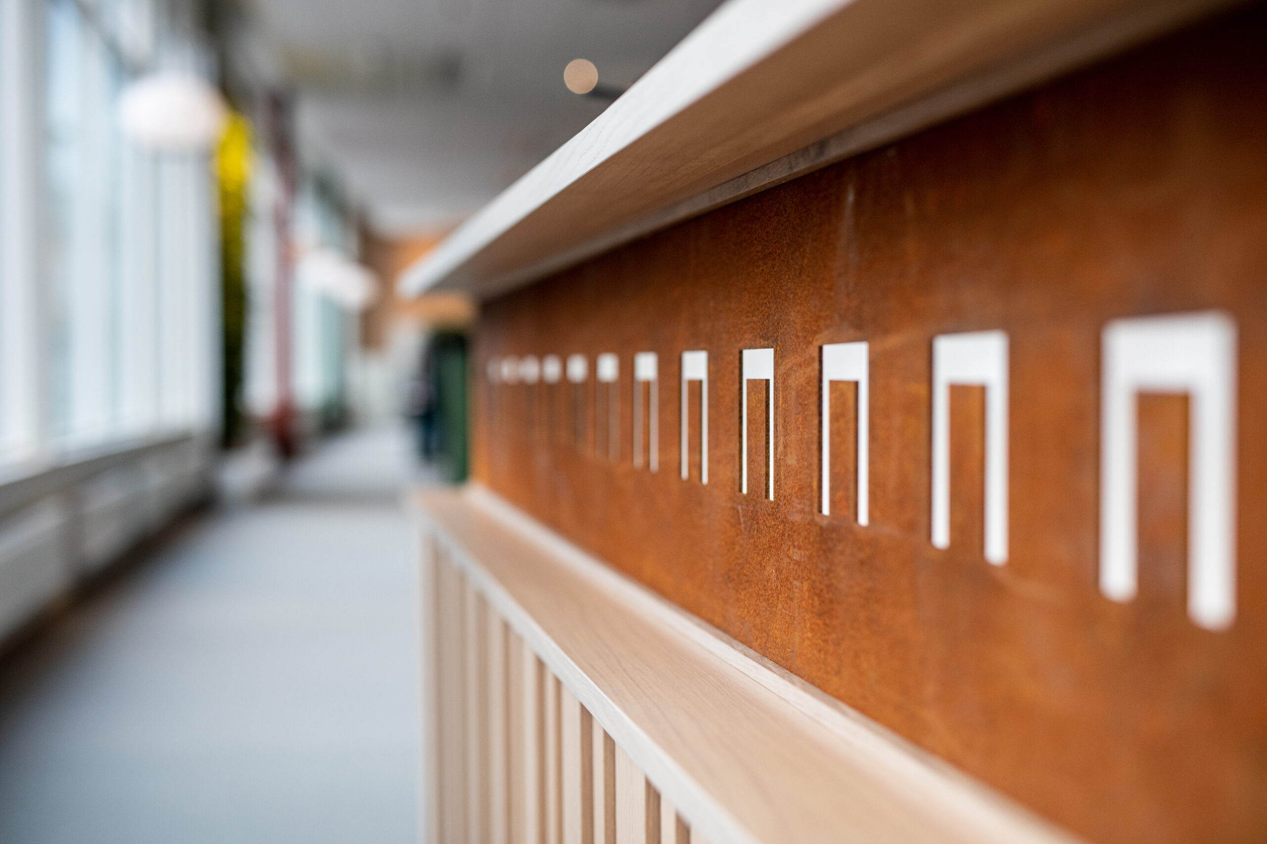 Detalj av foajé inredd med 100 procent återbruk: närbild på återbrukad trä- och metallpanel med utskurna grafiska former i en ljus, modern korridor.